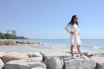 Fototapeta na wymiar Beautiful woman in white dress standing on the stone near the sea