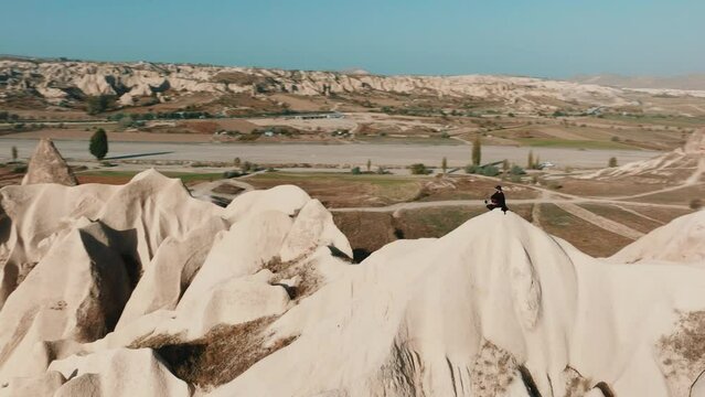 A man wear black t-shirt and hat sittning in Cappadocia rocks, drone footage