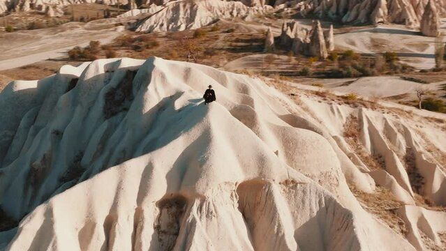 A man wear black t-shirt and hat sittning in Cappadocia rocks, drone footage