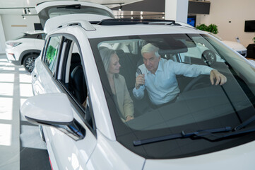 Fototapeta na wymiar Mature Caucasian couple sitting in a new car and rejoicing at the purchase. View through the windshield. 