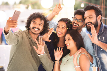 Group of friends talking on video call or chat during evening party gathering on terrace - concept...