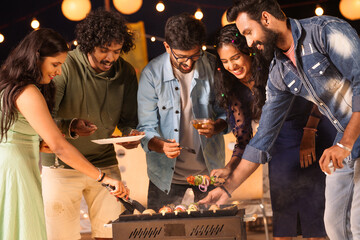 Group of friends busy cooking barbecue grills for dinner during night party - concept of togetherness, birthday gathering and celebration - obrazy, fototapety, plakaty