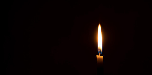 A single burning candle flame or light glowing on a small orange candle on black or dark background on table in church for Christmas, funeral or memorial service with copy space