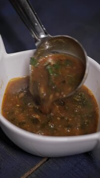 Female hand pouring indian spicy curry with moringa leaves in white bowl