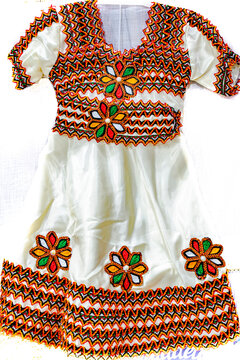 A traditional Algerian kabyle dress in white isolated on a white background. Flower patterns with petals in different colors,wave embroidery with black, red and orange threads.