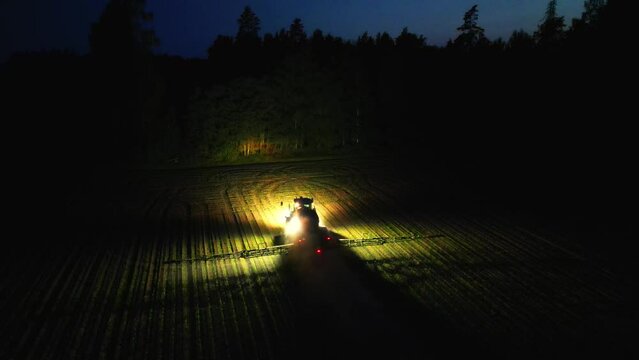 Night harvest, Aerial view captures the combine harvester working diligently, illuminating the fields, loading maize into trailers a vital scene in the agricultural supply chain 