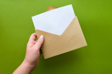 A hand holds a envelope with a blank sheet of paper. Letter template on green background