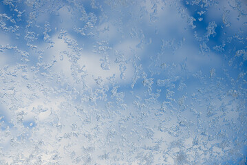 glass of roof window with frosted snowflakes and blue sky with clouds behind