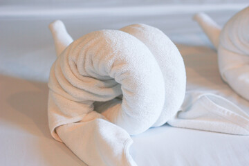 Fototapeta na wymiar White towels on the bed in the hotel room are rolled up into the shape of an elephant's head. Soft, vintage tones.