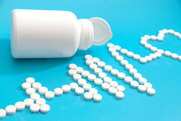 An electrocardiogram made of white tablets with a heart symbol. Blue background. A white pill jar. The concept of cardiac medicines.