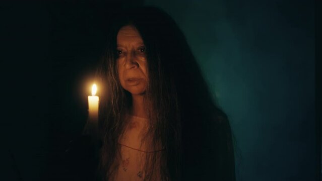 Possessed black witch holding burning candle and casting spells in haunted house
