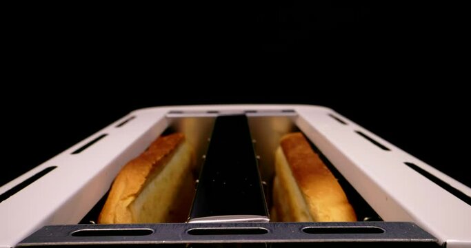 Extreme close-up of bread cooking in a toaster with toast flying in slow motion on a black background without people.