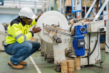 African male engineer in engine room Sit and use your hands to inspect plastic and steel roll...