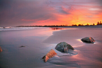 the setting pink and yellow sun casts golden light over the still beach and atlantic ocean at White...