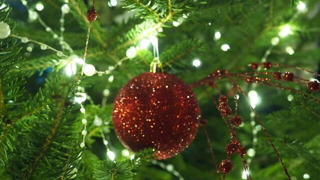 Decorations of christmas tree. Red glass bauble. Happy New Year Christmas tree. Beautiful ball on branch. Bokeh of side flickering light bulbs garlands for family winter holiday. Festival mood. Noel.