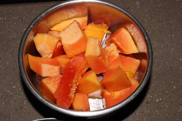 Orange small pieces of papita or papaya in a steel bowl on a brown marble floor, under flash