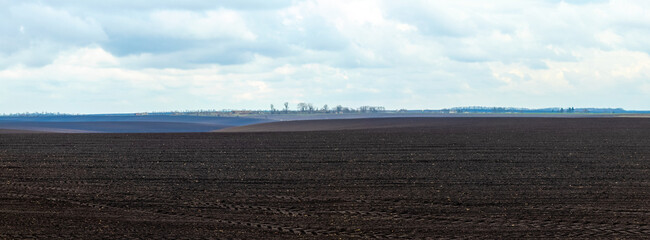 A plowed field in spring with a cloudy sky. Agricultural lands