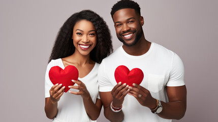 Smiling couple in white shirts, holding red heart-shaped objects, symbolizing love and togetherness.