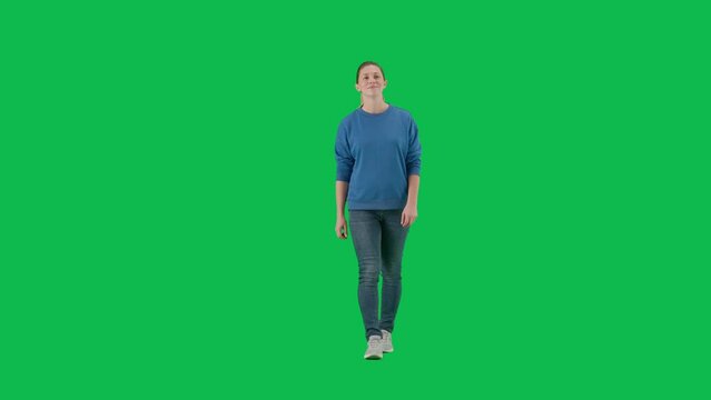 Front view of a young woman in full height walking on a green screen. A woman wearing sneakers, blue jeans and a hoodie, walking with an easy smile on her face, looking around.