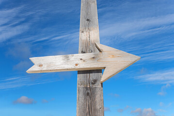 Wooden arrow on a post, with blue cloudy sky in the background