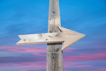 Fototapeta premium Wooden arrow on a post, with soft sunset sky in the background
