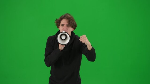Male activist with raised fist shouting menacingly into megaphone in studio on green screen. Front view of a pro protest man close up. Protest action, fight for human rights, strike.