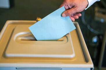 Stimmabgabe im Wahlbüro: Nahaufnahme der Hand eines Mannes, der seinen Stimmzettel in die Wahlurne steckt, viel Copy Space
