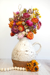 Dried flower arrangement in a ceramic jug. Displayed on a tabled with a white background. Wooden...
