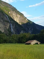 Waterfall in the mountains, Norway. Summer landscape with wooden house in the middle of a field
