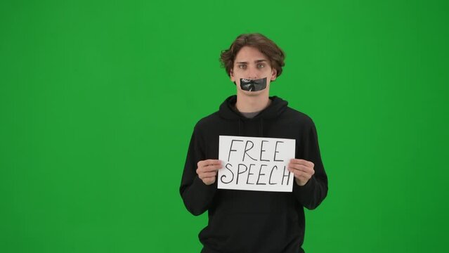 A man with his mouth taped with black tape holds a poster with the inscription Free speech. A Protestant man with a placard shrugs his shoulders in the studio on the green screen close up.