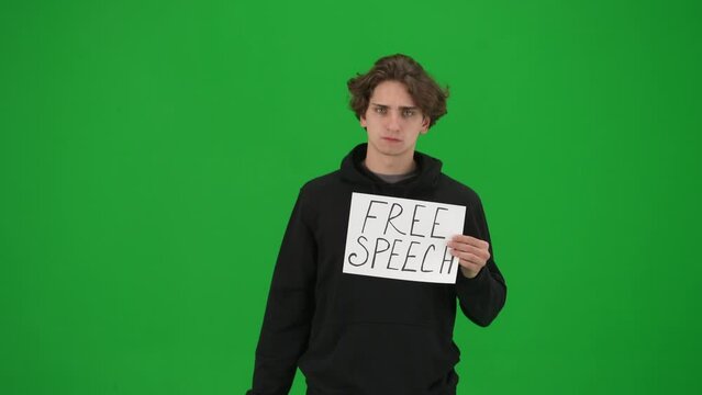A man with his mouth taped with black tape holds a poster with the inscription Free speech, close up. Protestant man removing tape from his mouth on green screen. Concept of freedom of speech.