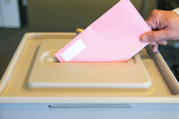 Stimmabgabe im Wahlbüro: Nahaufnahme der Hand eines Mannes, der seinen Stimmzettel in die Wahlurne...