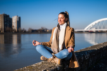 Beautiful woman enjoys meditating by the river  on a sunny winter day.