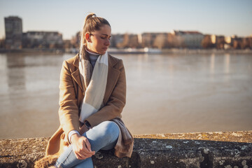 Sad woman sitting by the river. Toned image.