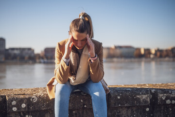 Worried woman having headache while sitting by the river. Toned image.