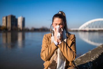Woman blowing nose  while sitting by the river on a sunny winter day.