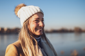 Close up portrait of natural beautiful woman in warm clothing enjoys spending time by the river on a sunny winter day. Toned image.