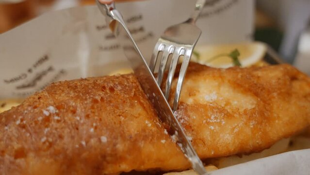 chef skillfully slices through golden-brown perfection crispy fish and chips. Each cut unveils the succulent interior, captures the essence of this beloved dish. High quality 4k footage