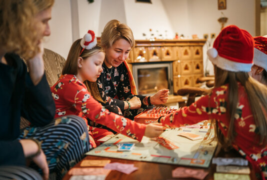 Mother with son and daughters kids playing together table board game, wearing Christmas hats. Cozy pre Christmas evening time moment. Family values, board games and X-mas celebration concept.