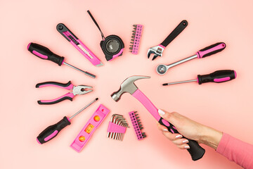 Renovation tools in the hands of a girl. Men's work is done by women's hands. Strong, but beautiful independent woman. Pink construction equipment in female hands on pink background. Woman's power