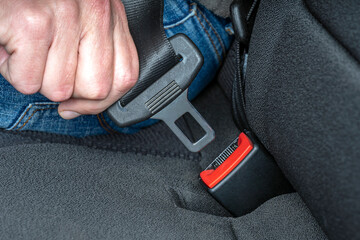 Close up of hand fastening seat belt buckle. Safety driving in car traveling.