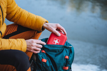 A guy puts a first aid kit in a backpack, packing things for a hike, safety in a winter trip, trekking in the mountains. personal first aid kit. - obrazy, fototapety, plakaty
