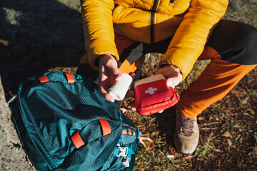 First aid kit in the hands of a man on a hike, a roll of elastic bandage, first aid in the mountains, survival in the forest. - obrazy, fototapety, plakaty