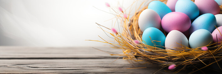 Colorful easter eggs nestle amidst golden straw and pink flowers on a wooden surface.