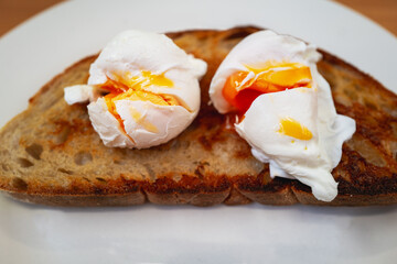 Two broken poached eggs with golden yolks on a slice of buttered toasted crispy sourdough bread. - 700805630