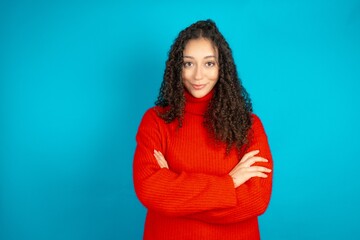 Dreamy Beautiful teen girl wearing knitted red sweater over blue background rest relaxed crossing...