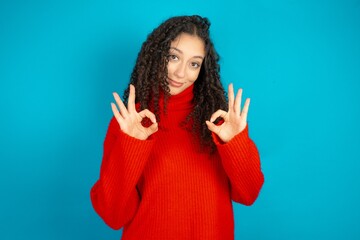 beautiful teen girl wearing red knitted sweater showing both hands with fingers in OK sign....