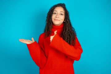 beautiful teen girl wearing red knitted sweater Showing palm hand and doing ok gesture with thumbs...
