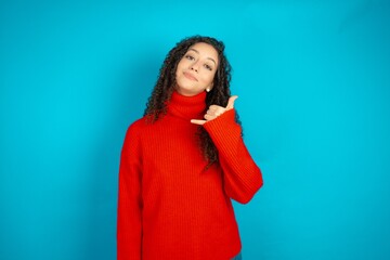 beautiful teen girl wearing red knitted sweater smiling doing phone gesture with hand and fingers like talking on the telephone. Communicating concepts.