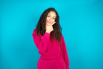 Young beautiful teen woman looking confident at the camera smiling with crossed arms and hand raised on chin. Thinking positive.